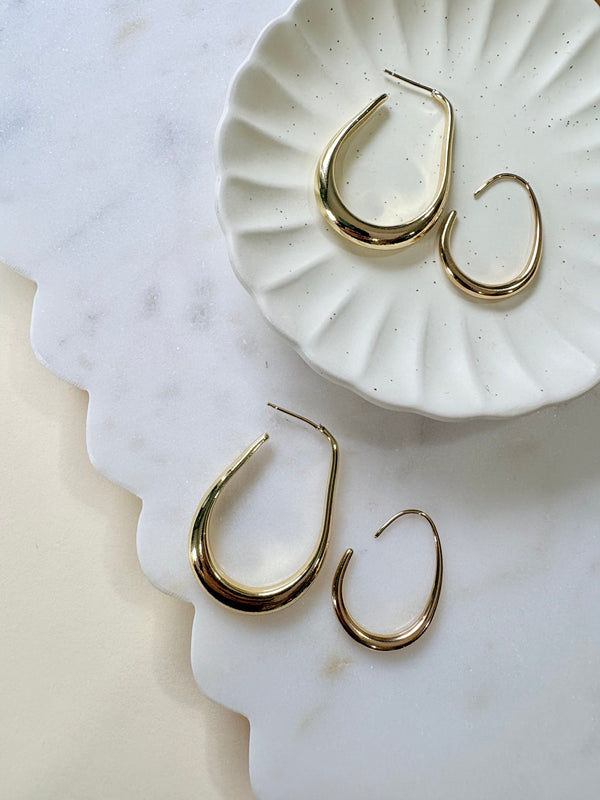 Gold hoop earrings on a white textured dish with a marble surface